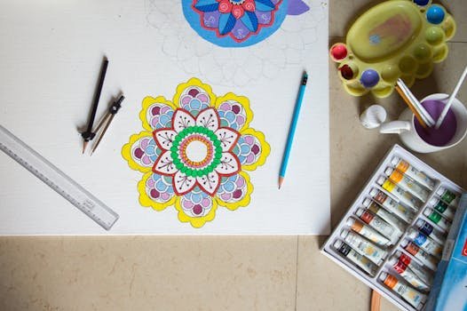 Vibrant mandala drawing with pencils, paint, and tools arranged neatly on a workspace.