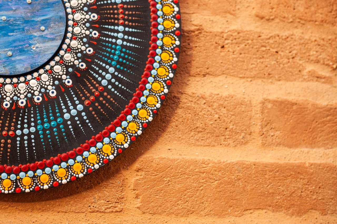 A vibrant circular mandala artwork with colorful patterns hanging on a textured brick wall.