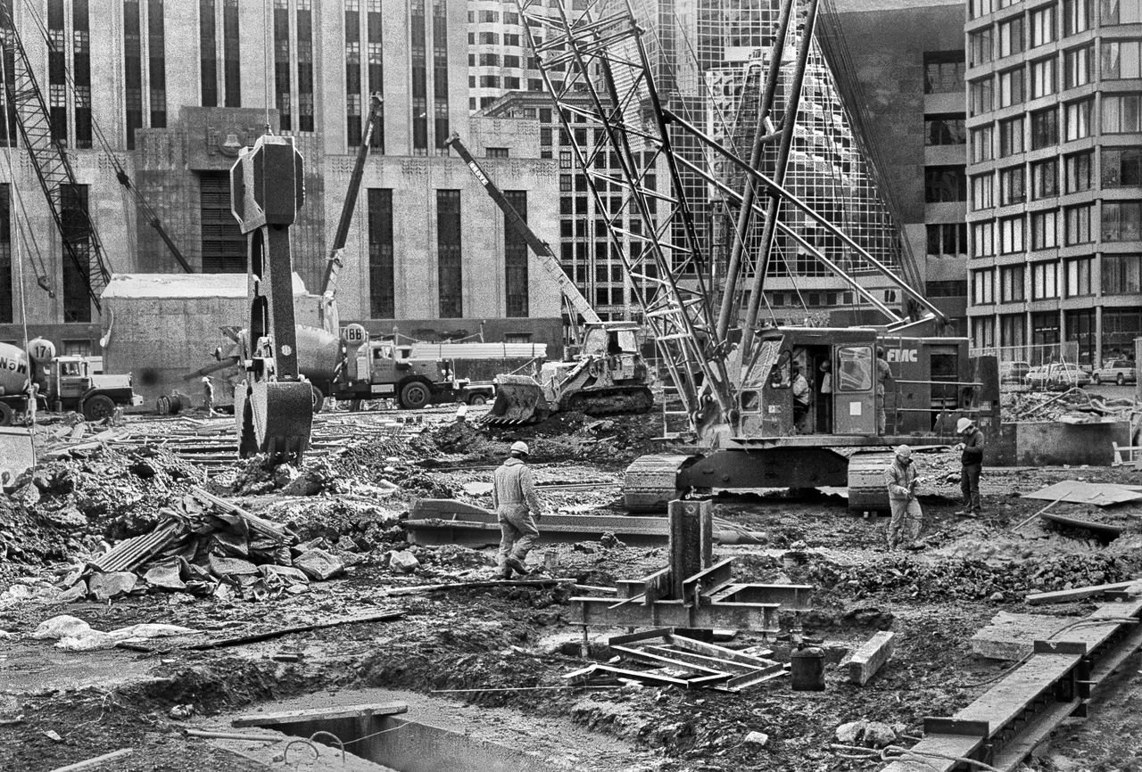 Black and white of faceless coworkers in protective helmets and workwear working on construction in city