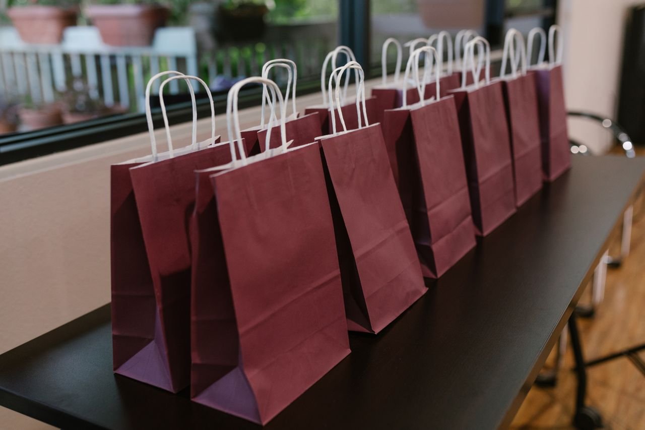 Purple paper bags with handles lined up on a table indoors, perfect for events.